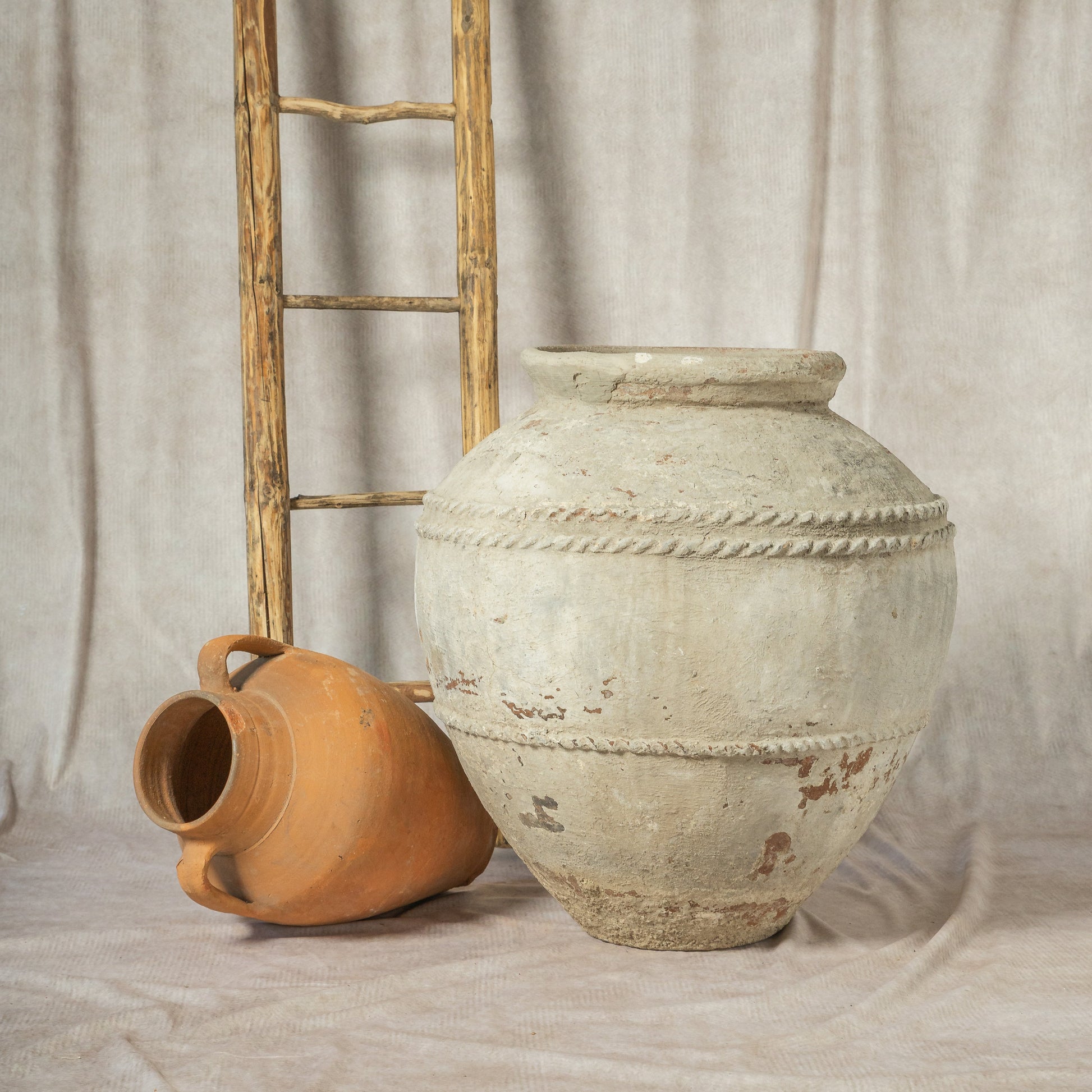 Two rustic pots, one terracotta and one ceramic, against a plain curtain background.